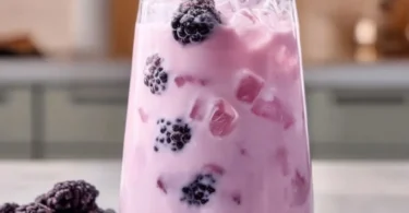 Homemade blackberry coconut pink drink served in a glass with fresh berries and coconut